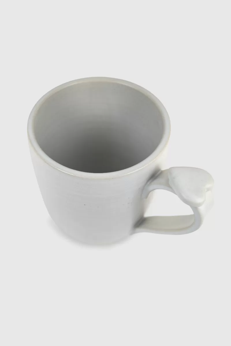 Tasse en grès blanc mat avec cœur sur l'anse pour une touche d'amour. Faite à la main, elle ajoute sophistication à votre pause café ou thé.